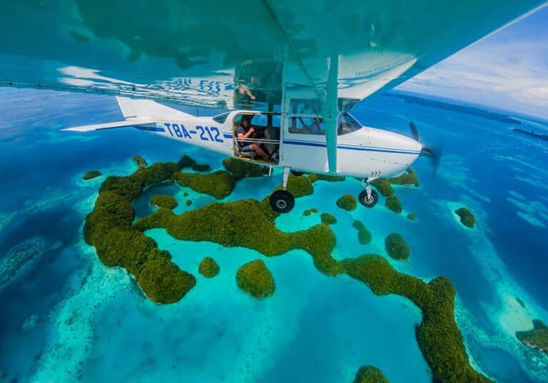 External mounted camera on underside of aircraft wing looking back at aircraft as it flies over tropical islands and lagoon in Palau, Micronesia